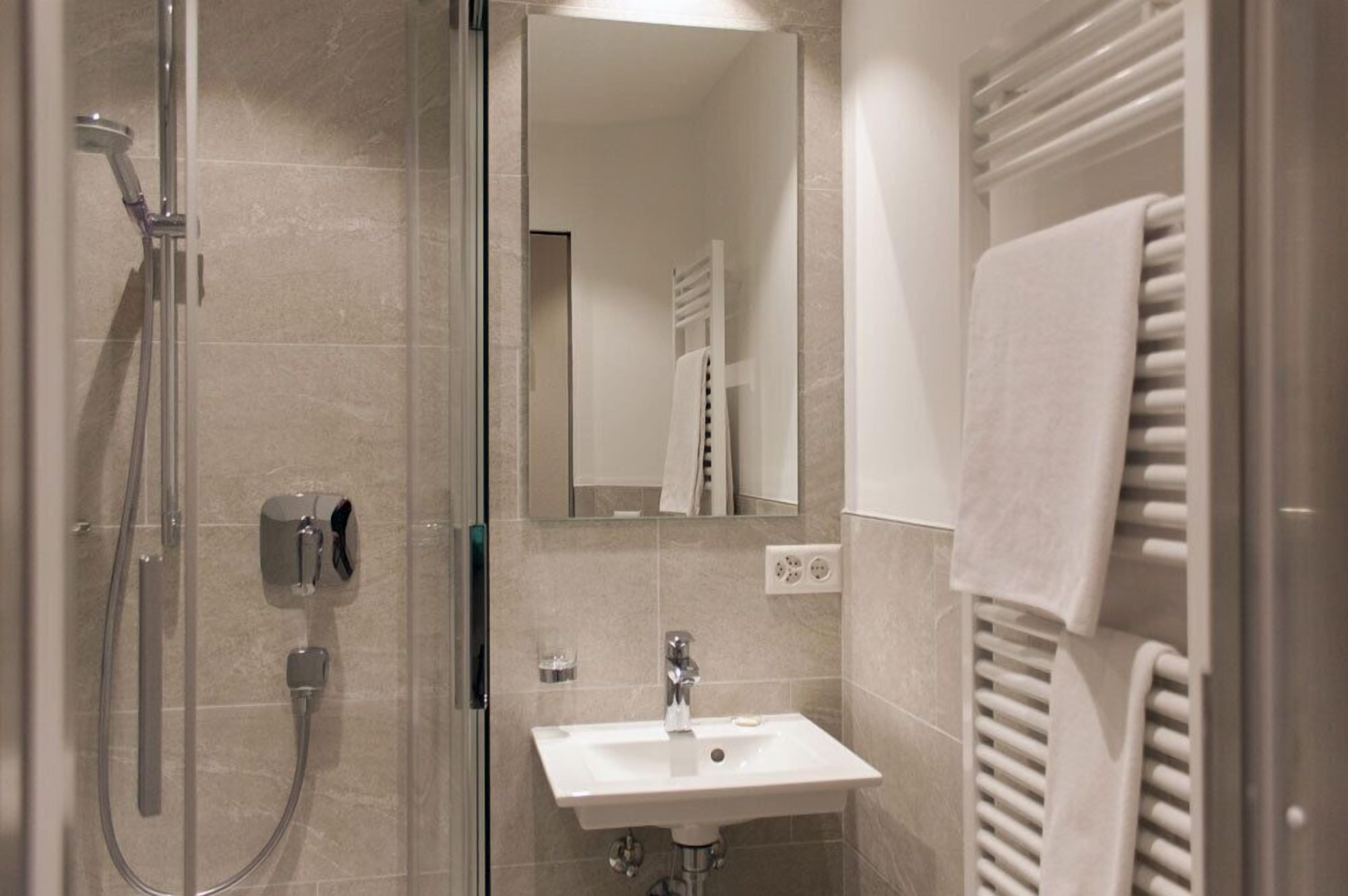 A modern bathroom with a glass shower enclosure, a white sink, and a towel rack.