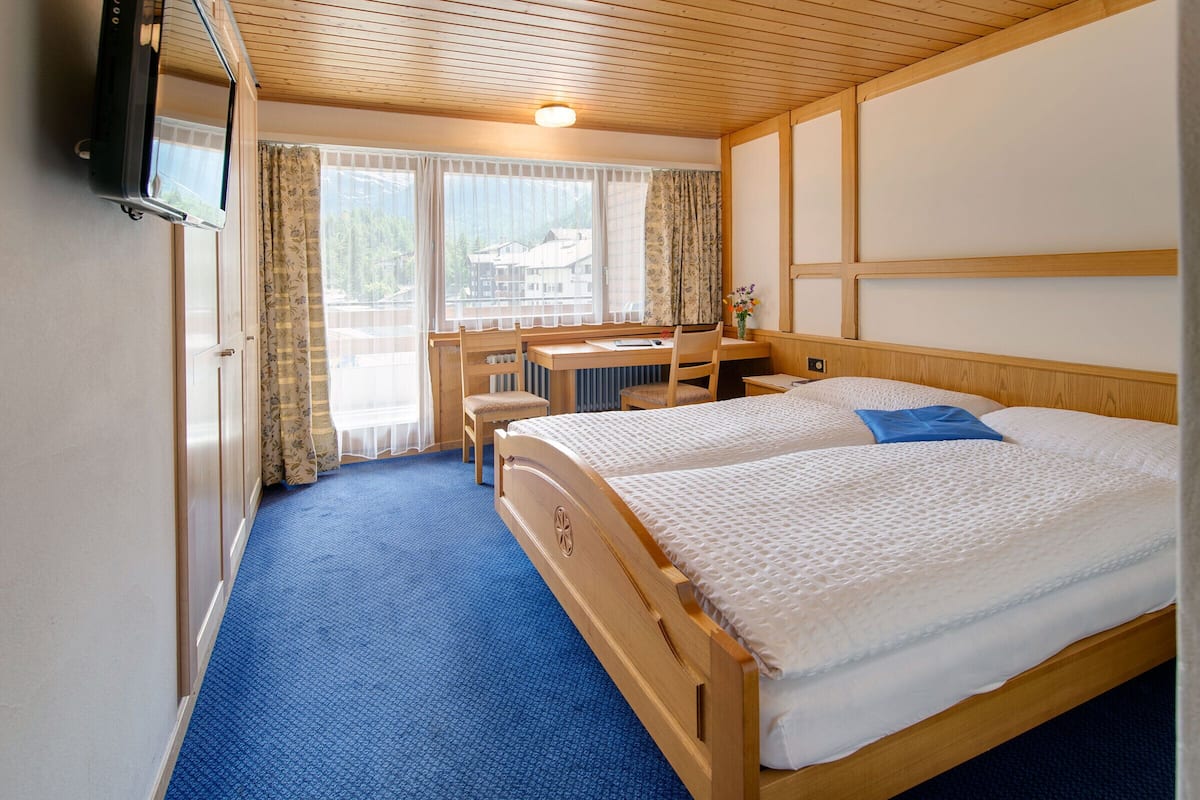 Quarto de hotel com duas camas, uma escrivaninha e uma televisão.