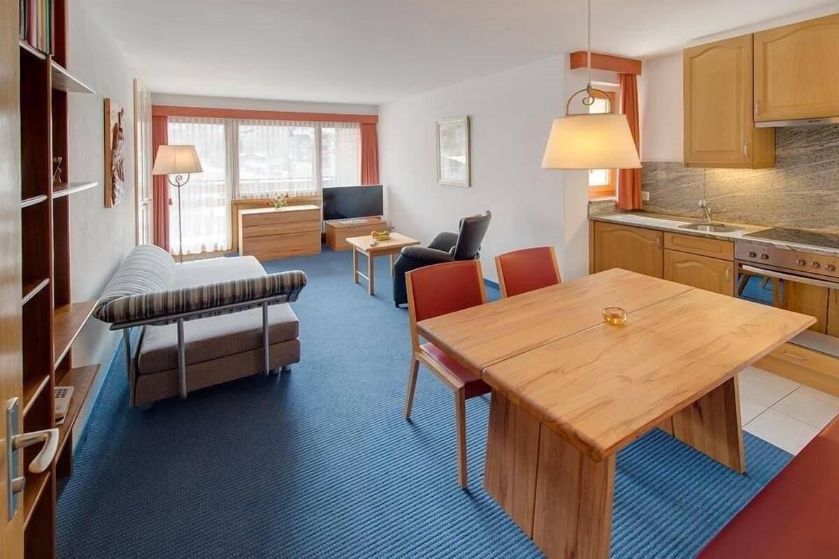 Quarto de hotel pequeno com cama, um sofá, uma mesa de jantar, televisão e cozinha compacta.