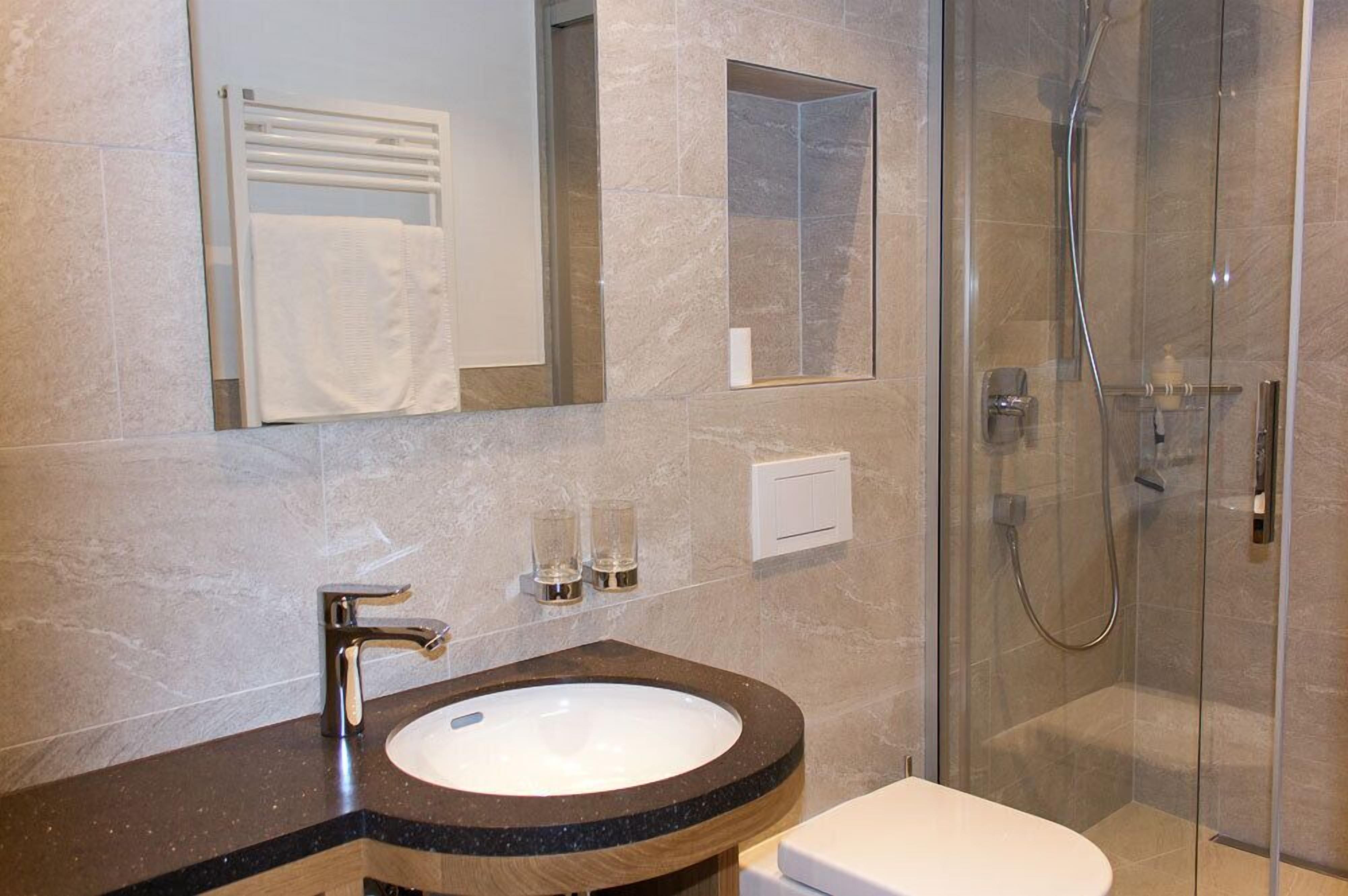 A bathroom with a marble sink, a mirror, a towel rack, and a glass-enclosed shower.