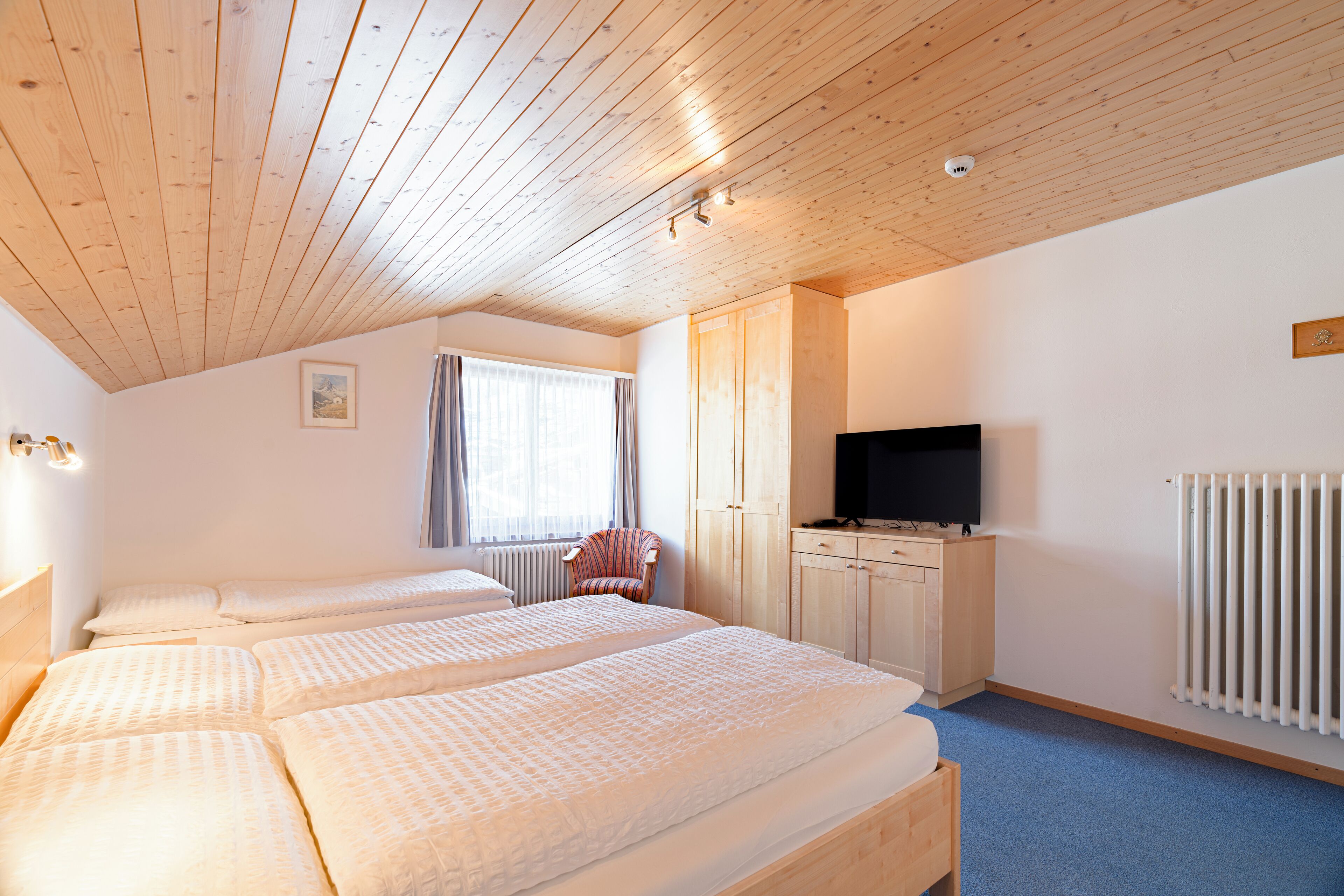 A bedroom with two beds, a television, a radiator, and wooden ceiling beams.