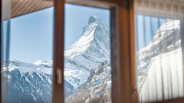 A mountain view through a window with wooden frames. - Hotel Parnass (Zermatt)