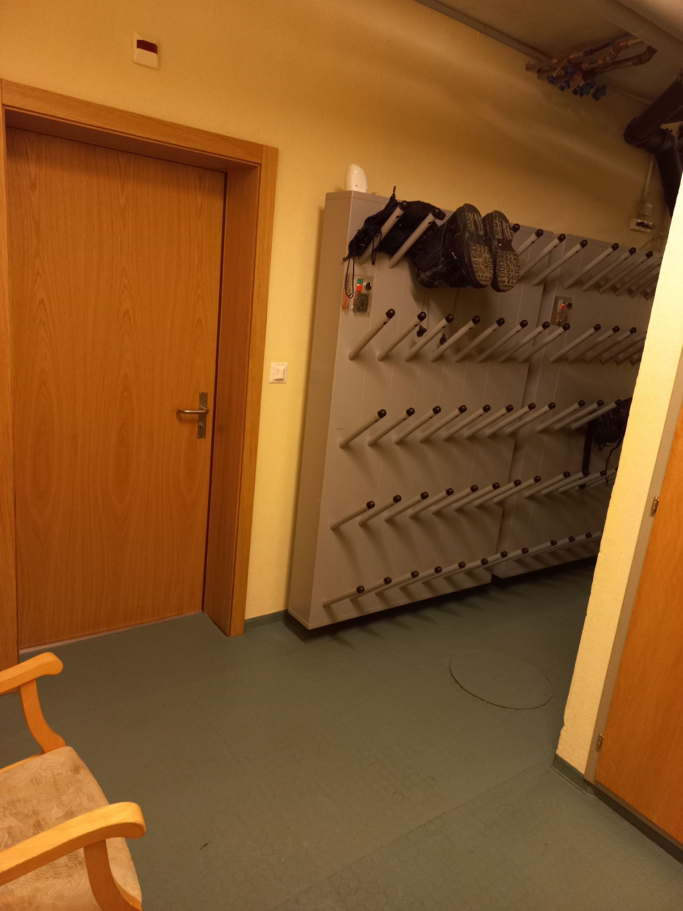 A room with a wooden door, a shoe rack with multiple pairs of shoes, and a chair.