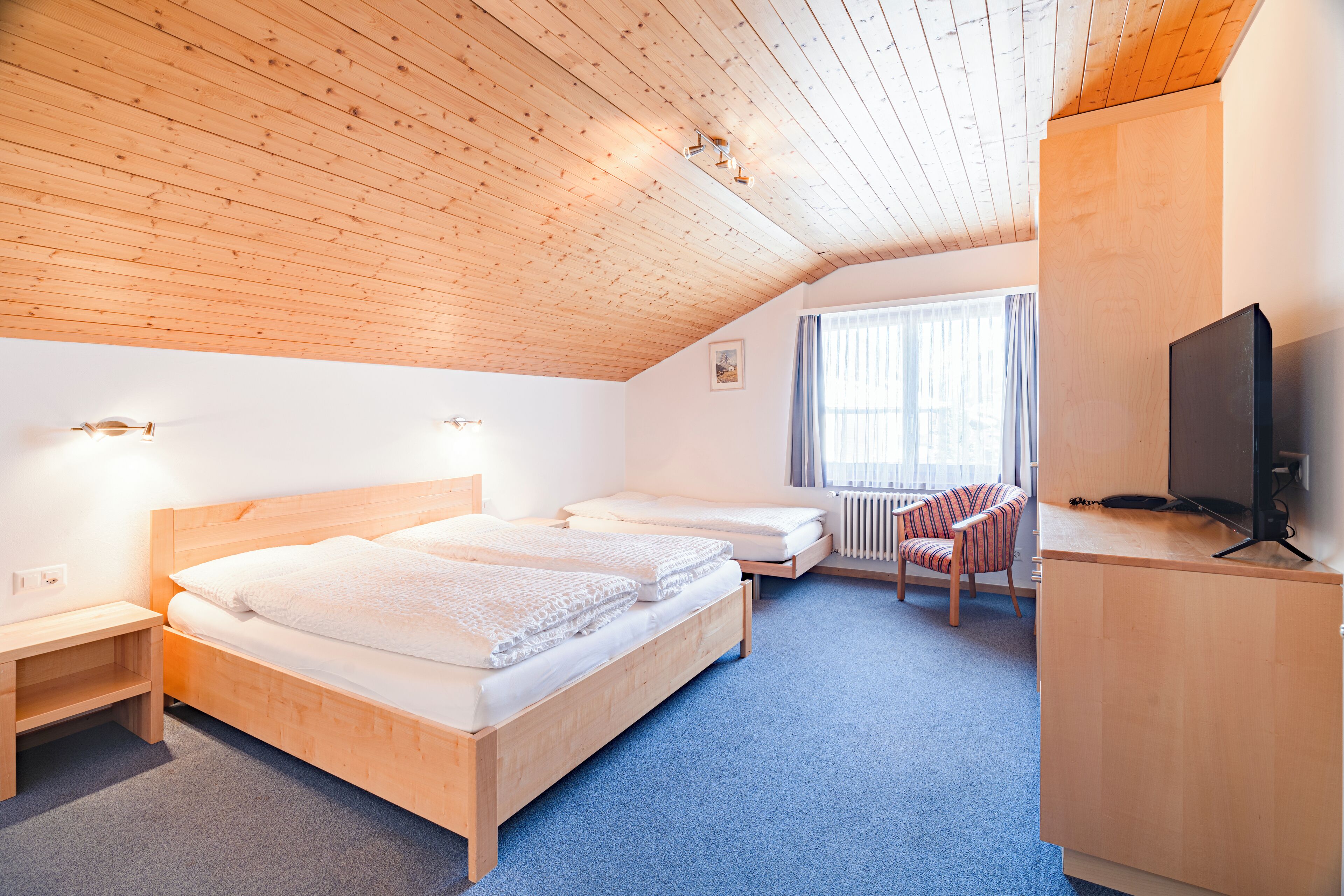 Une chambre avec deux lits en bois, un bureau avec une télévision, une chaise et une fenêtre avec des rideaux.