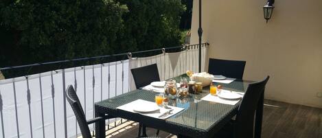 An outdoor dining area with a table set for two, surrounded by chairs, and an umbrella providing shade.
