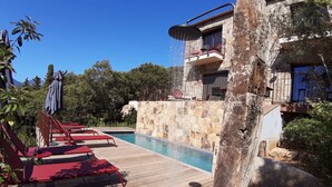 Un área de piscina con sillas de descanso rojas, una pared de piedra y un edificio con balcones.