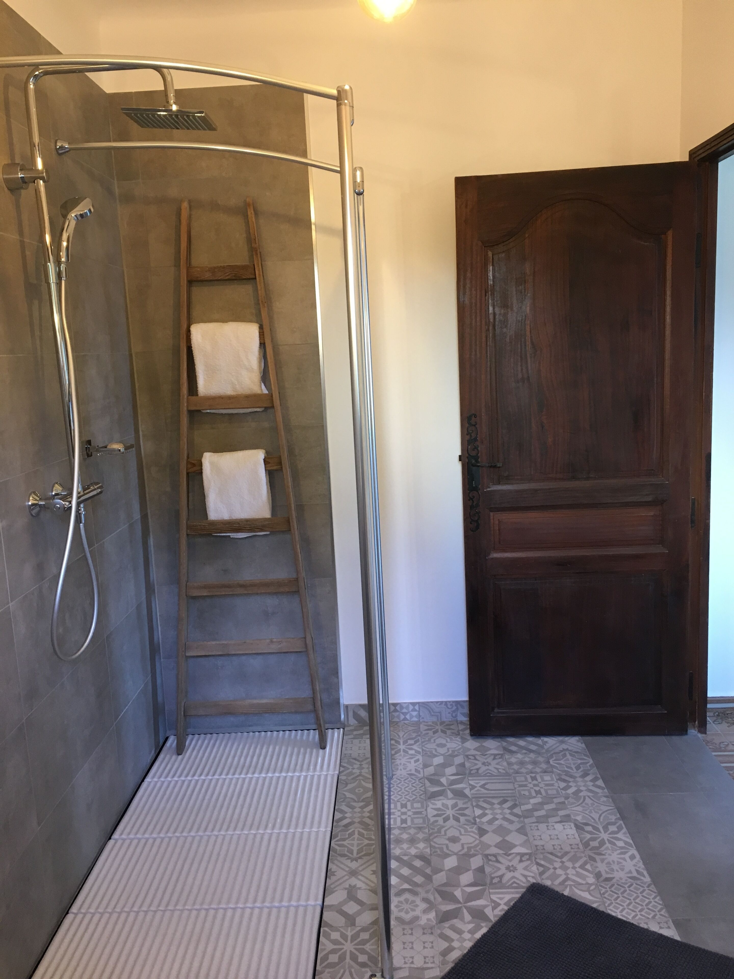 Un área de ducha con puerta de vidrio, una escalera metálica y una puerta de madera al fondo.