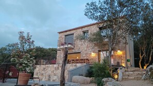 Un edificio de piedra con balcón, mobiliario exterior y un jardín con rocas y plantas.