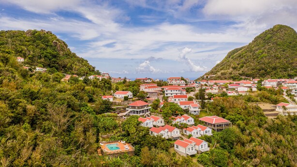 A hillside village with red-roofed houses, lush greenery, and a clear sky. - The Cottage Club Hotel (Windward Side)