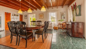 A dining area with a wooden table and chairs, hanging pendant lights, and a view of the outdoors. - The Cottage Club Hotel (Windward Side)