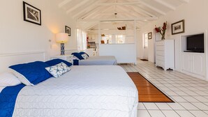 A hotel room with a large bed, a desk, a chair, a TV, and a ceiling fan. - The Cottage Club Hotel (Windward Side)