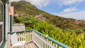 A balcony with a white chair and a white picket fence overlooking a hillside with houses and lush greenery. - The Cottage Club Hotel (Windward Side)