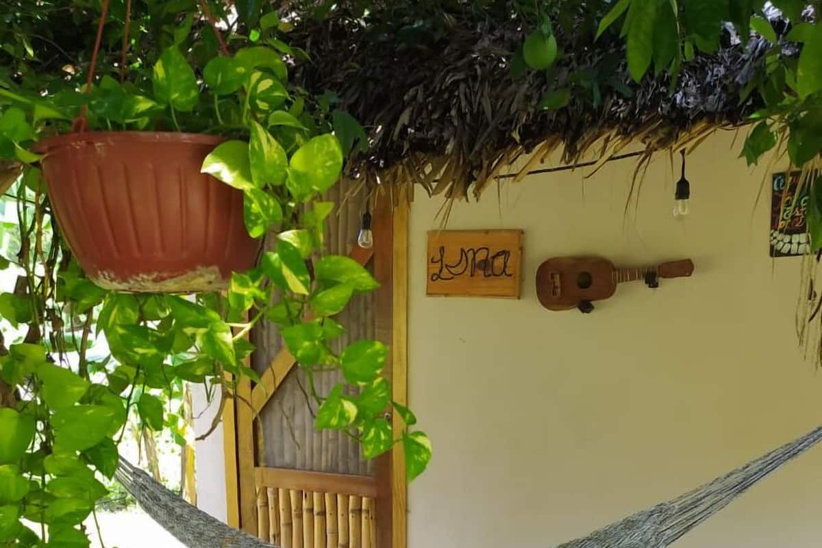 Eine Hängematte unter einem Reetdach, eine Holztür und eine Gitarre an der Wand.
