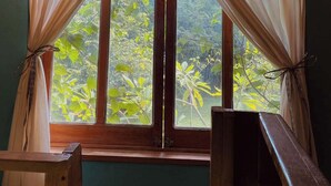 A room with a bed, a wooden chair, a window with curtains, and a hanging light fixture.