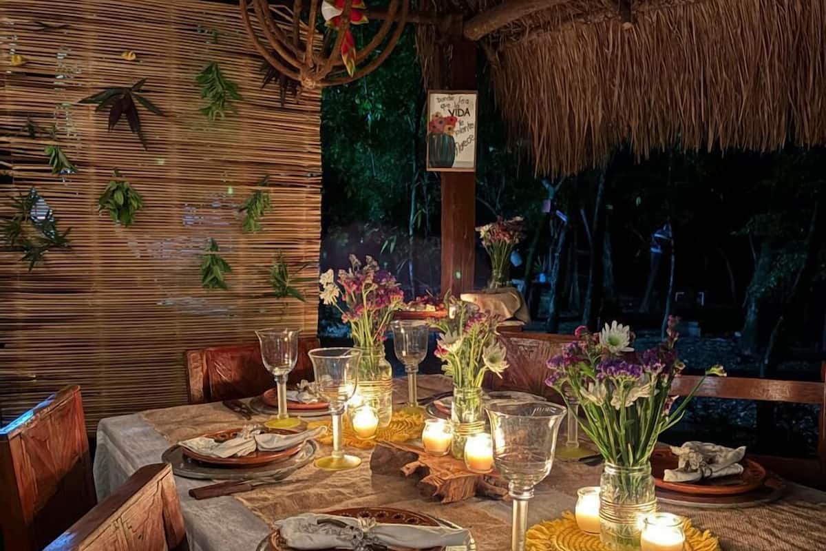 Ein Essbereich im Freien mit einem Reetdach, Holzsesseln und einem für eine Mahlzeit gedeckten Tisch.