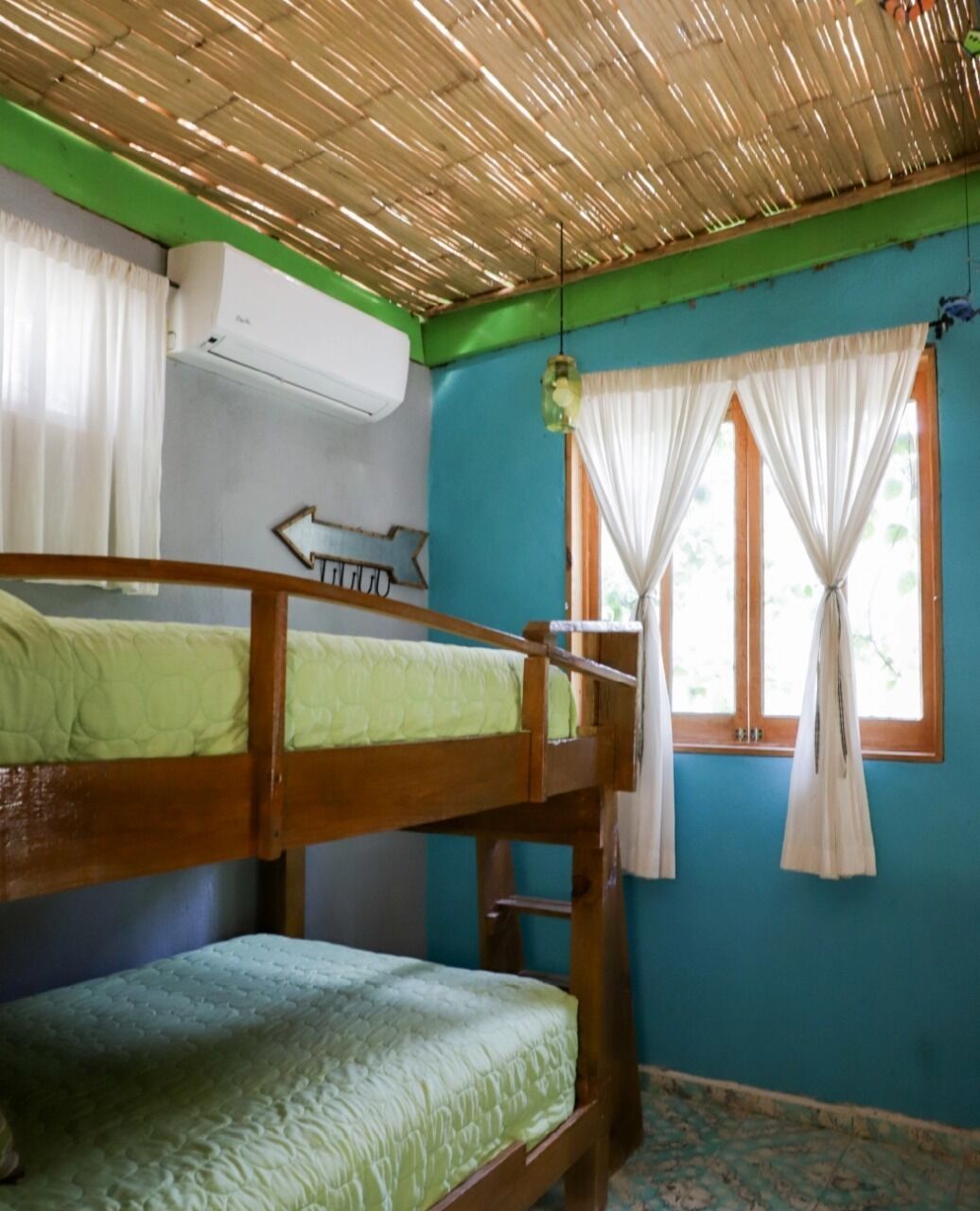 Una habitación con dos literas, una ventana con cortinas, una lámpara colgante y un equipo de aire acondicionado.