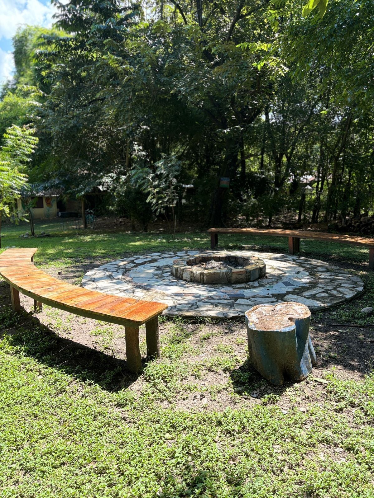 A circular stone fire pit surrounded by a wooden bench and a metal stool.