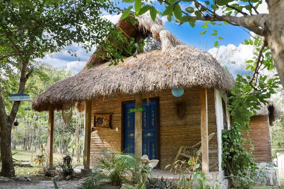 Eine rustikale Hütte mit Strohdach, einer blauen Tür und einem kleinen Garten mit Pflanzen und einer Statue.
