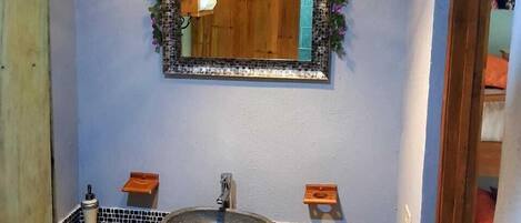 Un baño con un lavamanos de piedra, un tocador de madera, un espejo con una guirnalda floral y un aplique colgante.