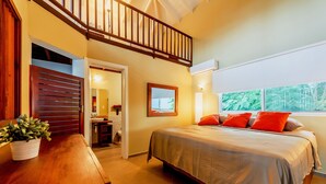 Une chambre à coucher avec un lit, un bureau en bois, une plante en pot, un escalier et une fenêtre donnant sur des arbres.