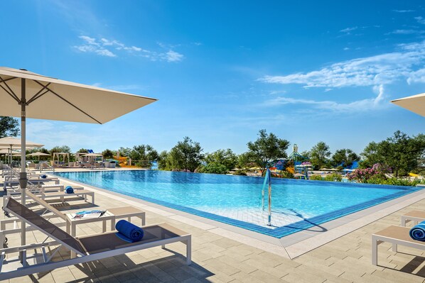 A swimming pool with lounge chairs and umbrellas, surrounded by trees and a clear sky. - Victoria mobilehome Istra Premium Camp (Funtana)