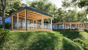 Una estructura moderna al aire libre con zona de estar cubierta y paredes de vidrio, rodeada de exuberante follaje y árboles.