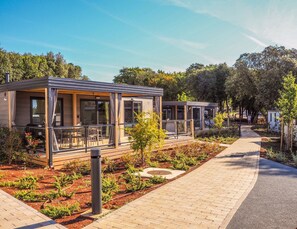 Uma fileira de cabanas modernas e compactas, com portas e janelas de vidro, rodeada por jardins bem cuidados e um caminho pavimentado.