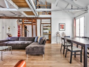 A modern living space with a sectional sofa, a dining table with chairs, and a staircase leading to an upper level. - Apartment at Paris - Le Marais - Bastille (Paris)