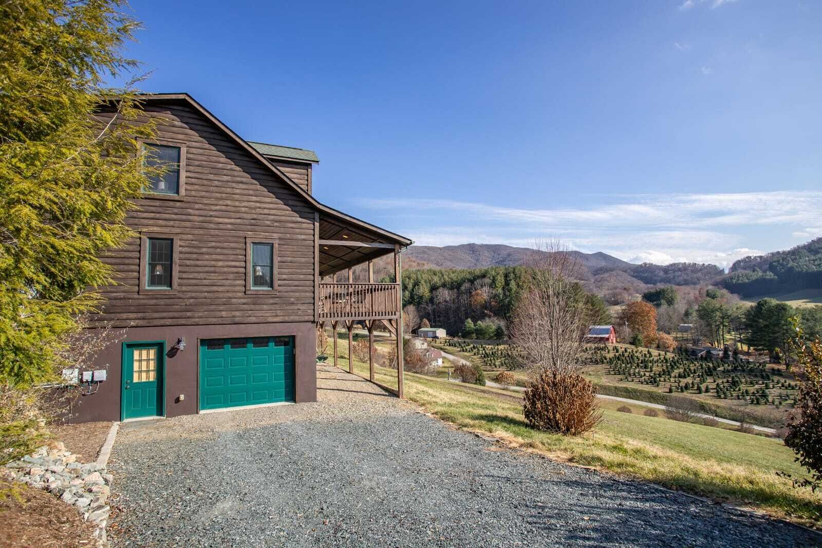 Una baita in legno a due piani con un portone garage verde, un portico coperto e vista su un paesaggio montuoso.