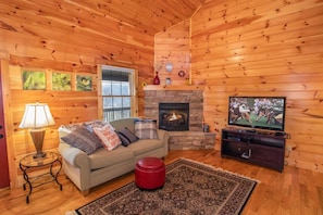 Ein gemütliches Blockhaushaus-Interieur mit Kamin, einer Couch, einem Fernseher und einem Teppich.