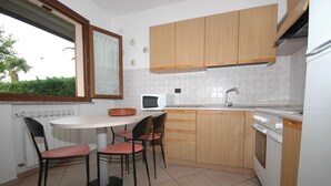 A compact kitchen with a dining table, chairs, a microwave, a sink, and wooden cabinets. - Two-room apartment Alex 1, 2 minutes drive from the beach (Marina di Campo)