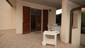 A covered patio area with a table and chairs, a white cart, and a sliding glass door leading to an interior space. - Two-room apartment Alex 1, 2 minutes drive from the beach (Marina di Campo)