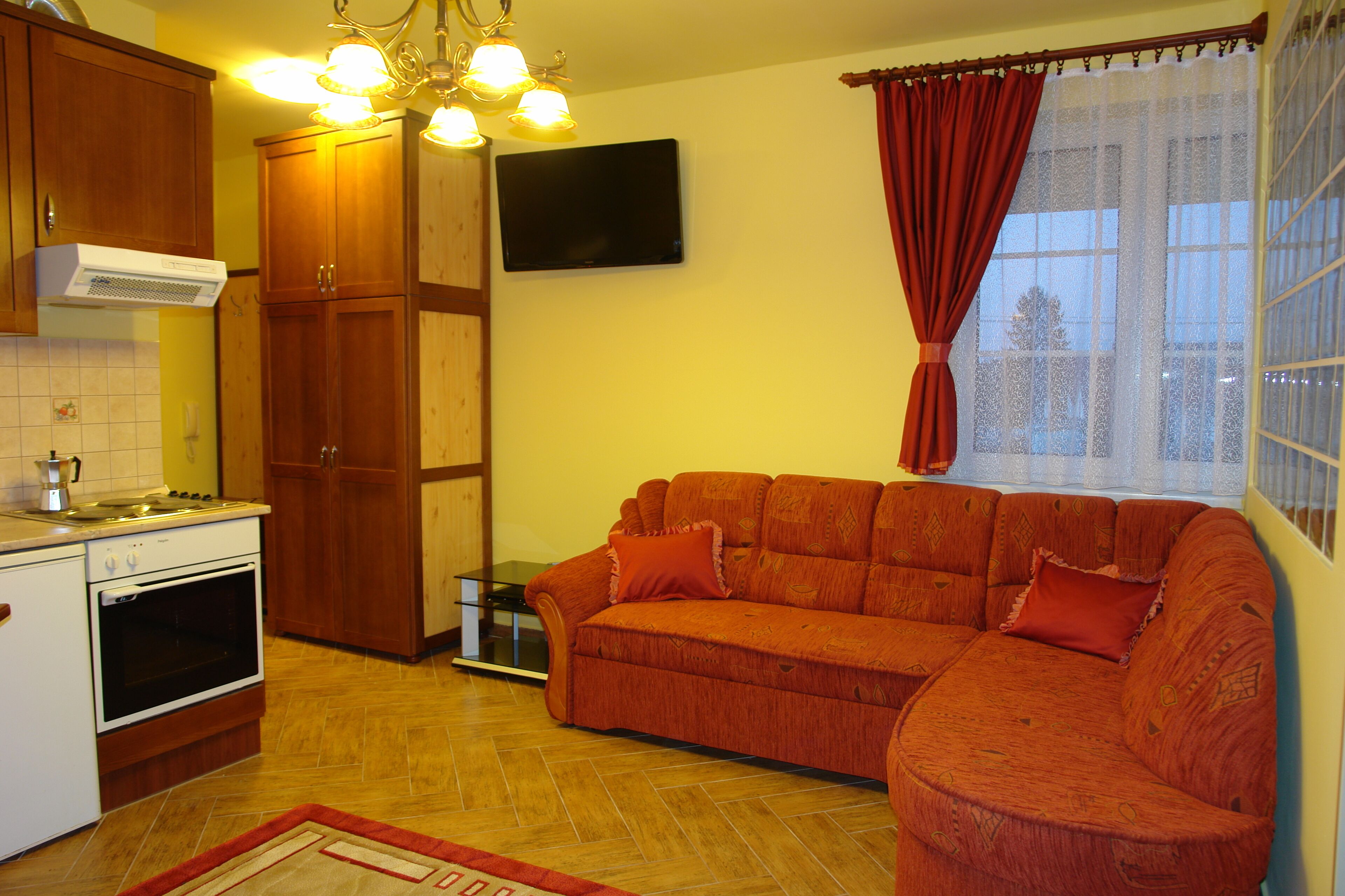A kitchen with wooden cabinets, a stove, and a television mounted on the wall.