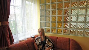 A person sitting on a red sofa in a room with a window and a patterned wall. - HoldLux Apartmanok (Sarvar)