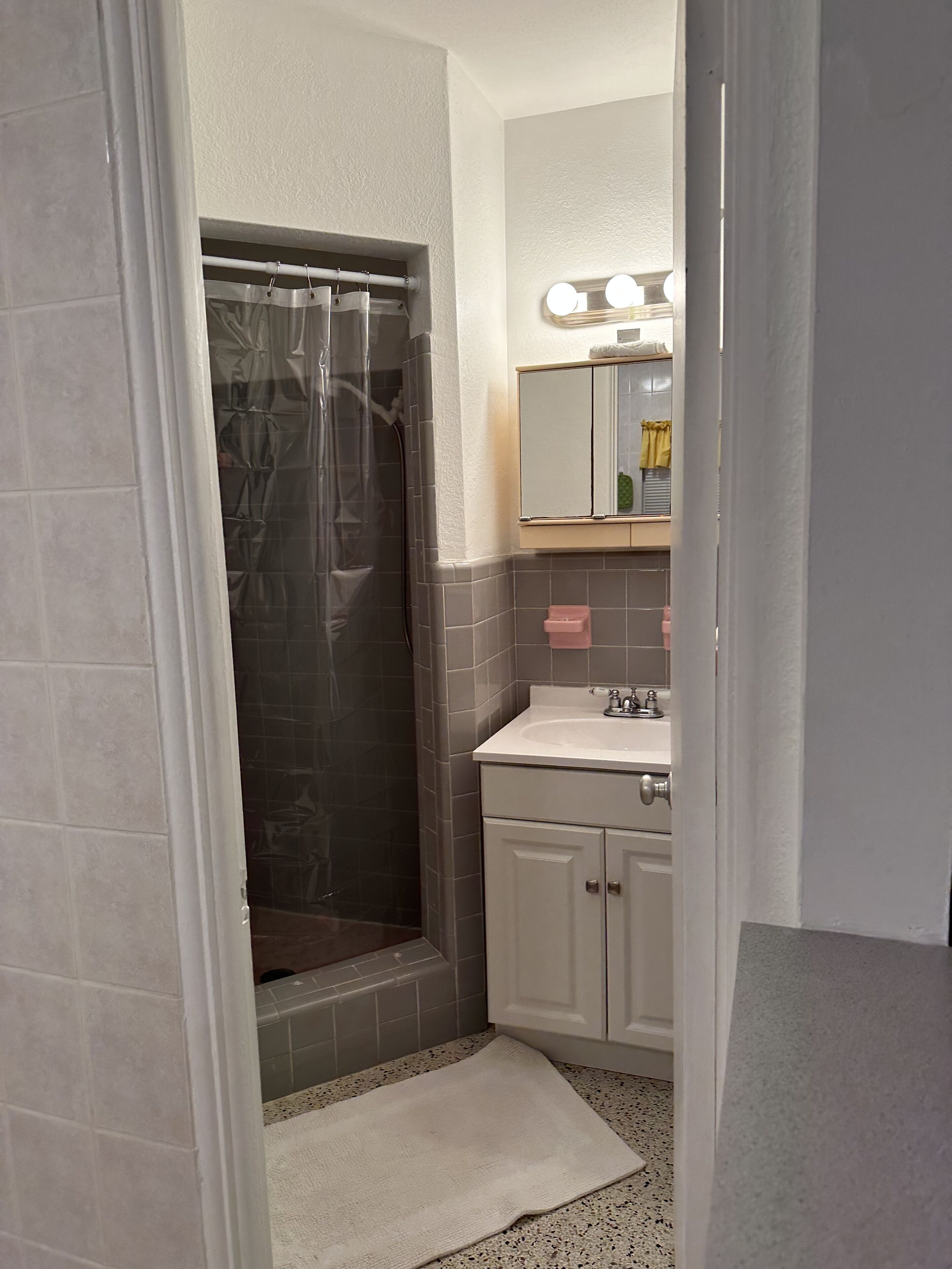 Ein Badezimmer mit Dusche, Waschbecken, einem beleuchteten Spiegel und einem Handtuch auf dem Boden.