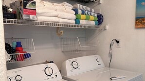 A laundry area with two front-loading washing machines, a shelf with folded towels, and a wall-mounted power outlet. - STEPS TO GULF BEACH! (Holmes Beach)