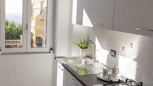 Une cuisine moderne avec des meubles blancs, une cuisinière à gaz et une fenêtre donnant sur un balcon.