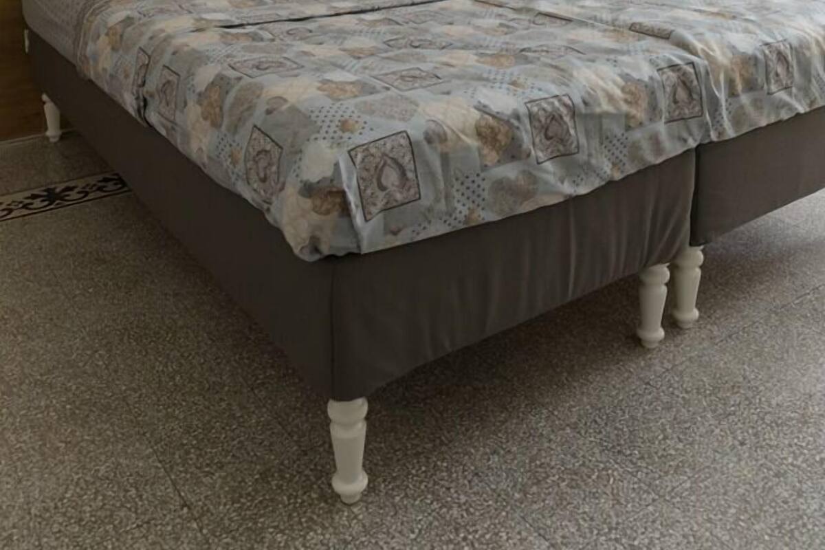 Une chambre à coucher avec une tête de lit en bois, un lit recouvert d’une literie à motifs et une petite table de chevet sur laquelle est posé un vase.