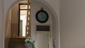 Un couloir avec un escalier, une horloge, un luminaire et une porte.