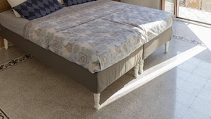 Une chambre à coucher avec une tête de lit en bois, un lit recouvert d’une literie à motifs, une petite table de chevet et une vue sur l’extérieur, visible à travers une porte-fenêtre coulissante.