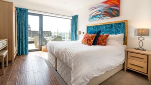A hotel room with a large bed, a desk, a chair, and a view of the city through the window. - Antrim House Guest Rooms & Suites (Portrush)