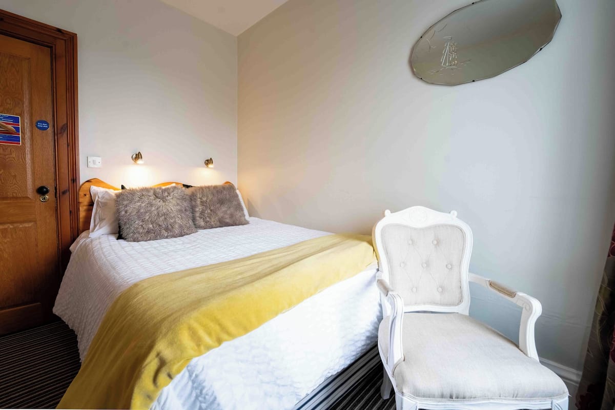 Une chambre d’hôtel avec un lit, une chaise, une porte et un luminaire fixé au mur.