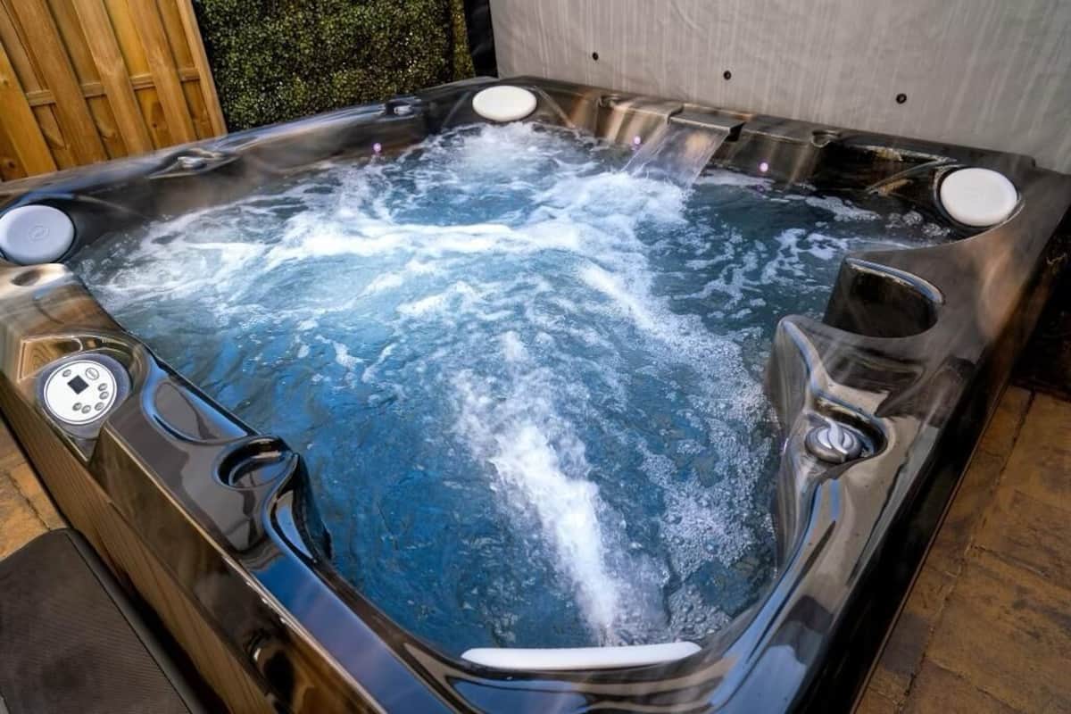 Un bain à remous doté de plusieurs jets, d’un panneau de commande et, en arrière-plan, d’une clôture en bois.