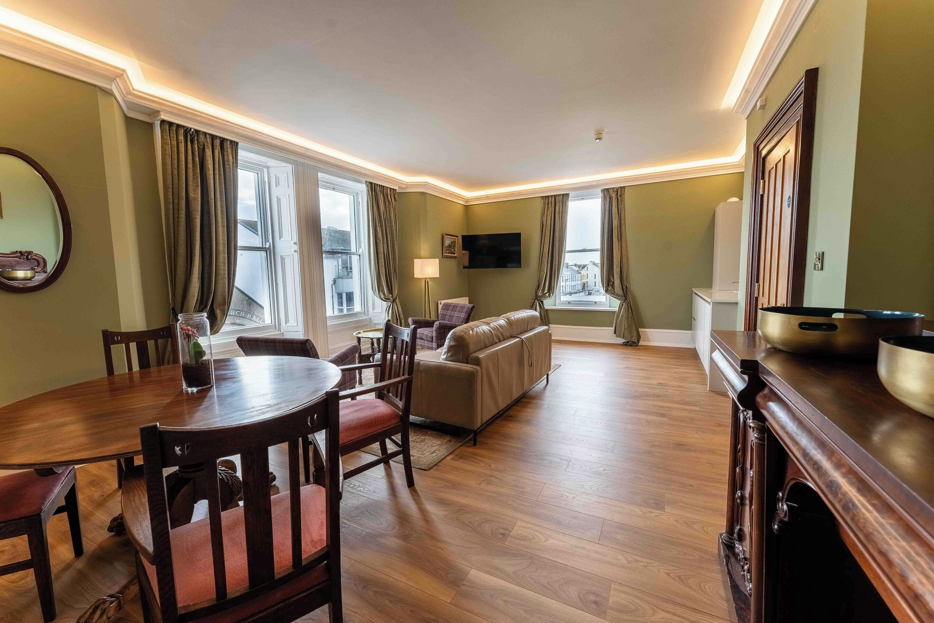 Een ruime woonkamer met een houten eettafel, een bank en een televisie die aan de muur is bevestigd.