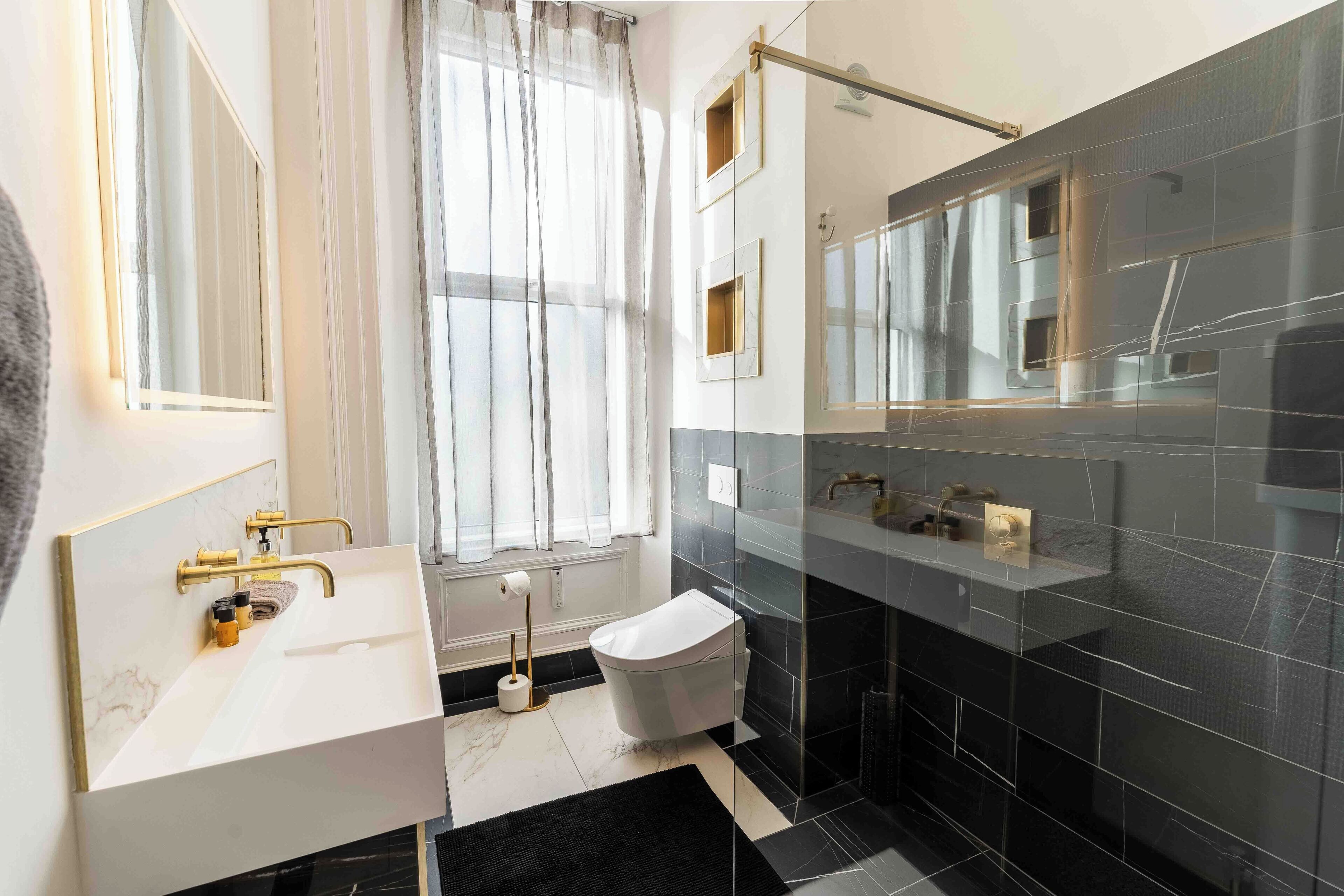 Et moderne badeværelse med en hvid vask, guldfarvede armaturer, et toilet og en brusekabine i glas.