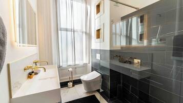 Un baño moderno con lavamanos blanco, grifería dorada, inodoro y cabina de ducha de vidrio.