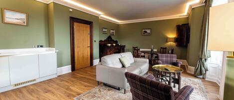 Una sala de estar con un sofá blanco, un sillón de cuadros, una mesa redonda y un comedor con mesa y sillas.