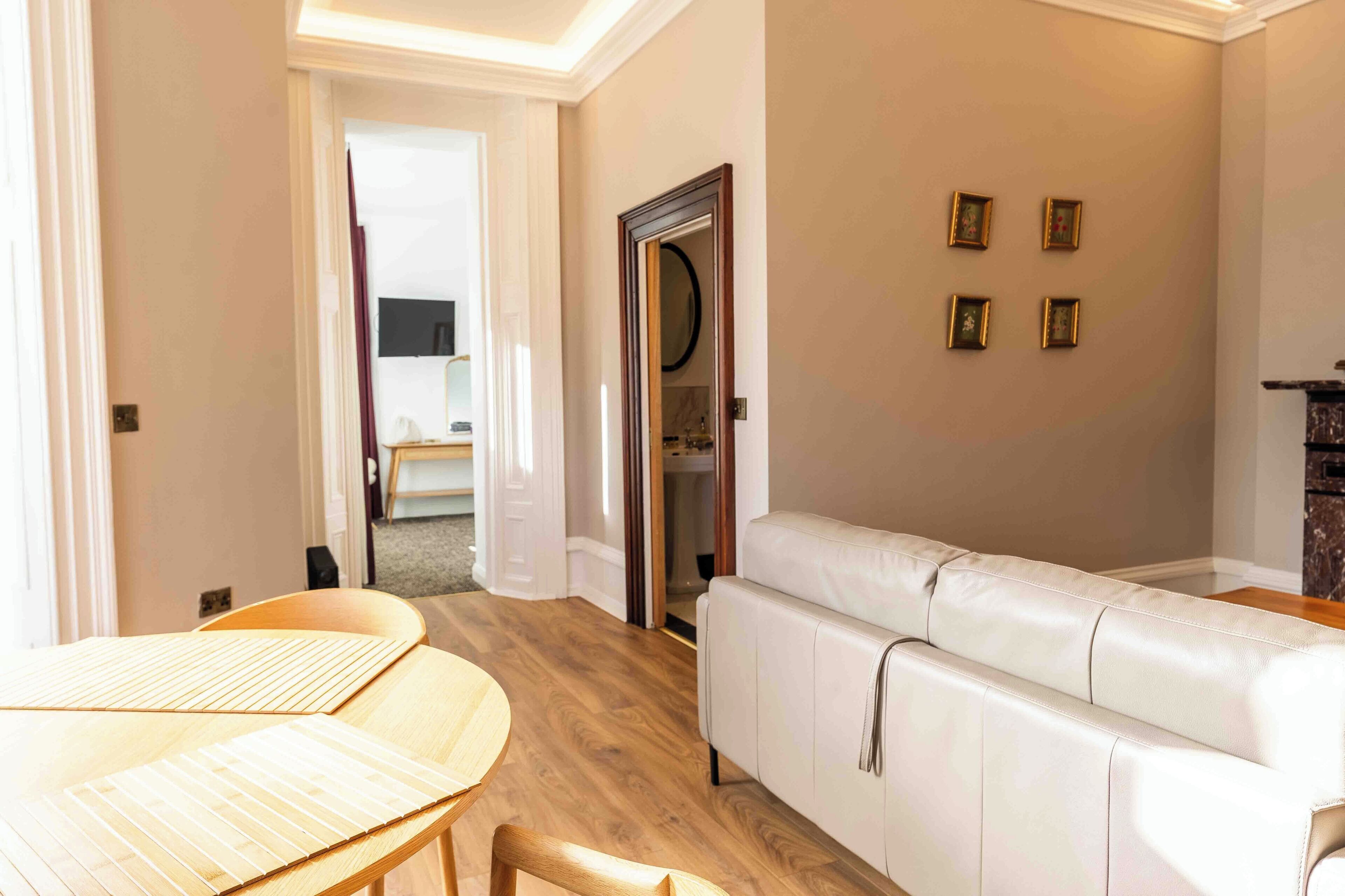 A modern living room with a white leather sofa, wooden flooring, and a dining area with a table and chairs.