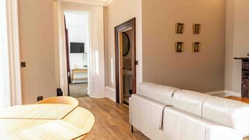 A modern living room with a white leather sofa, wooden flooring, and a dining area with a table and chairs.