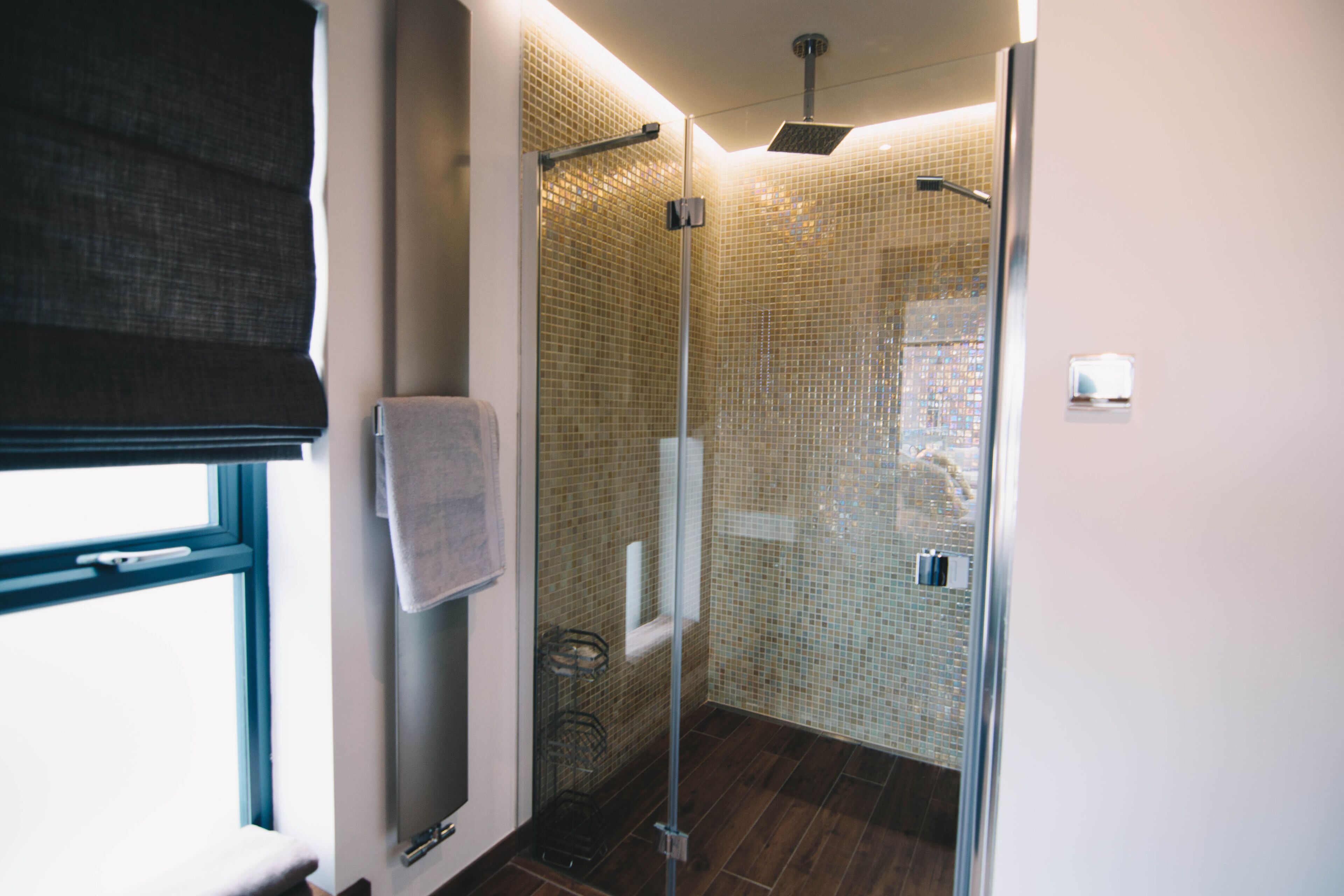 A modern bathroom with a glass shower enclosure, a towel rack, and a window with a view.